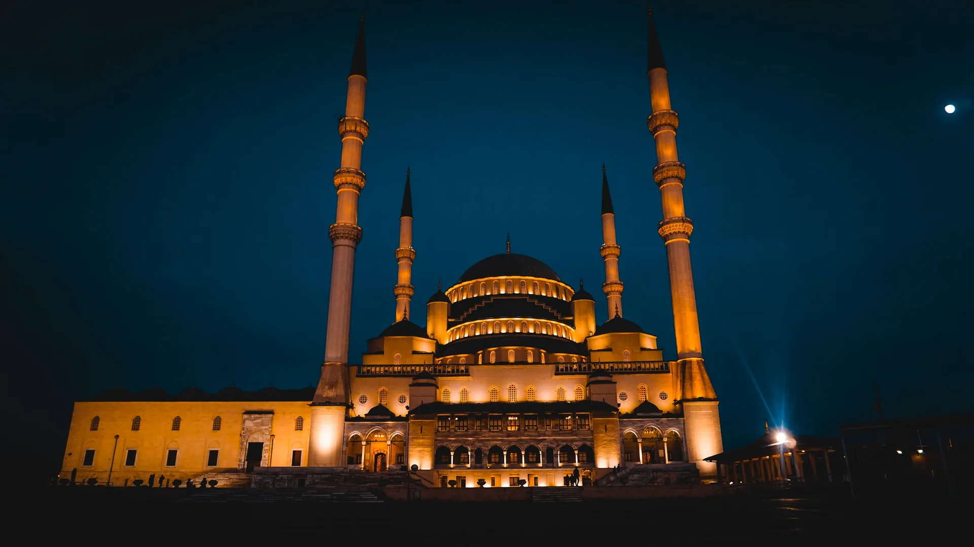 A domed masjid with twin minarets, floodlit against a deep blue night sky