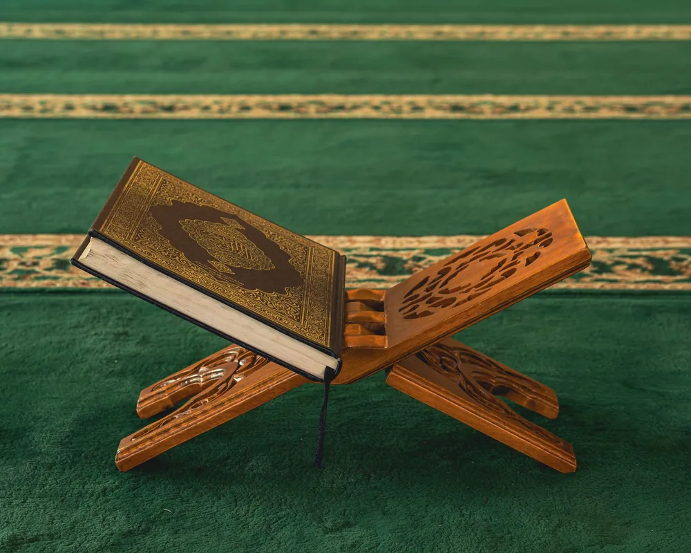 A Qurʾān resting on a carved wooden rehal on a green mosque carpet